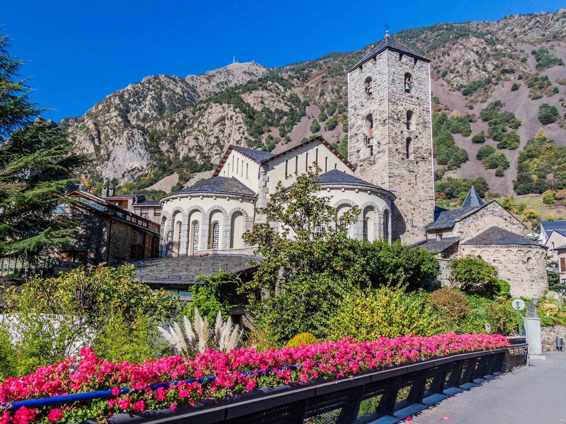 Blumenverzierte Brücke mit Blick auf die romanische Kirche Santa Coloma vor der beeindruckenden Kulisse der Pyrenäen in Andorra.