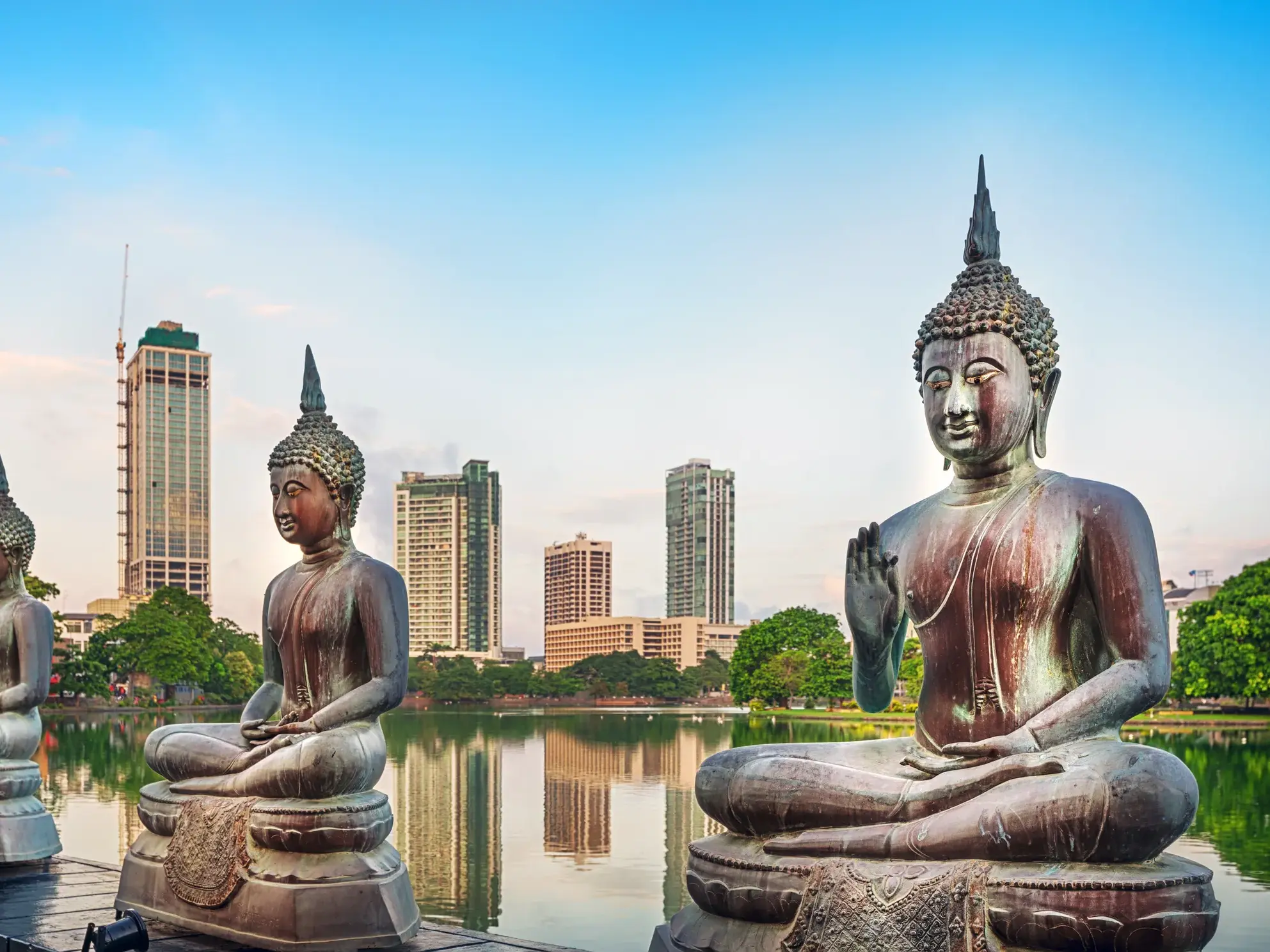 Meditierende Buddha-Statuen des Seema Malaka Tempels am Beira See vor der modernen Skyline von Colombo, Sri Lanka.